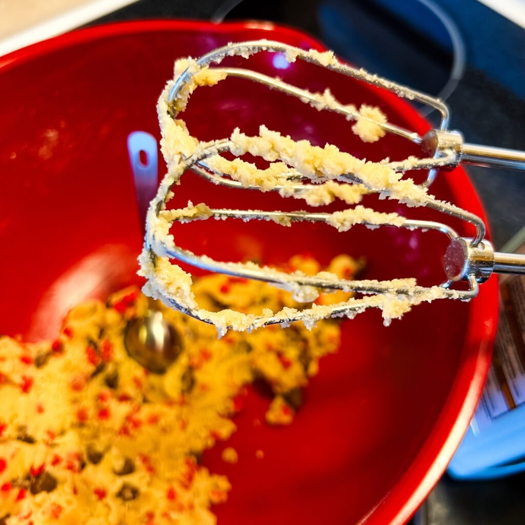 Mixing chocolate cherry chip cookie dough with a hand mixer.