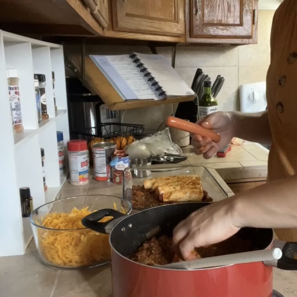 Dipping the Egglife wraps in chili before wrapping the hot dogs for the chili cheese dog casserole.