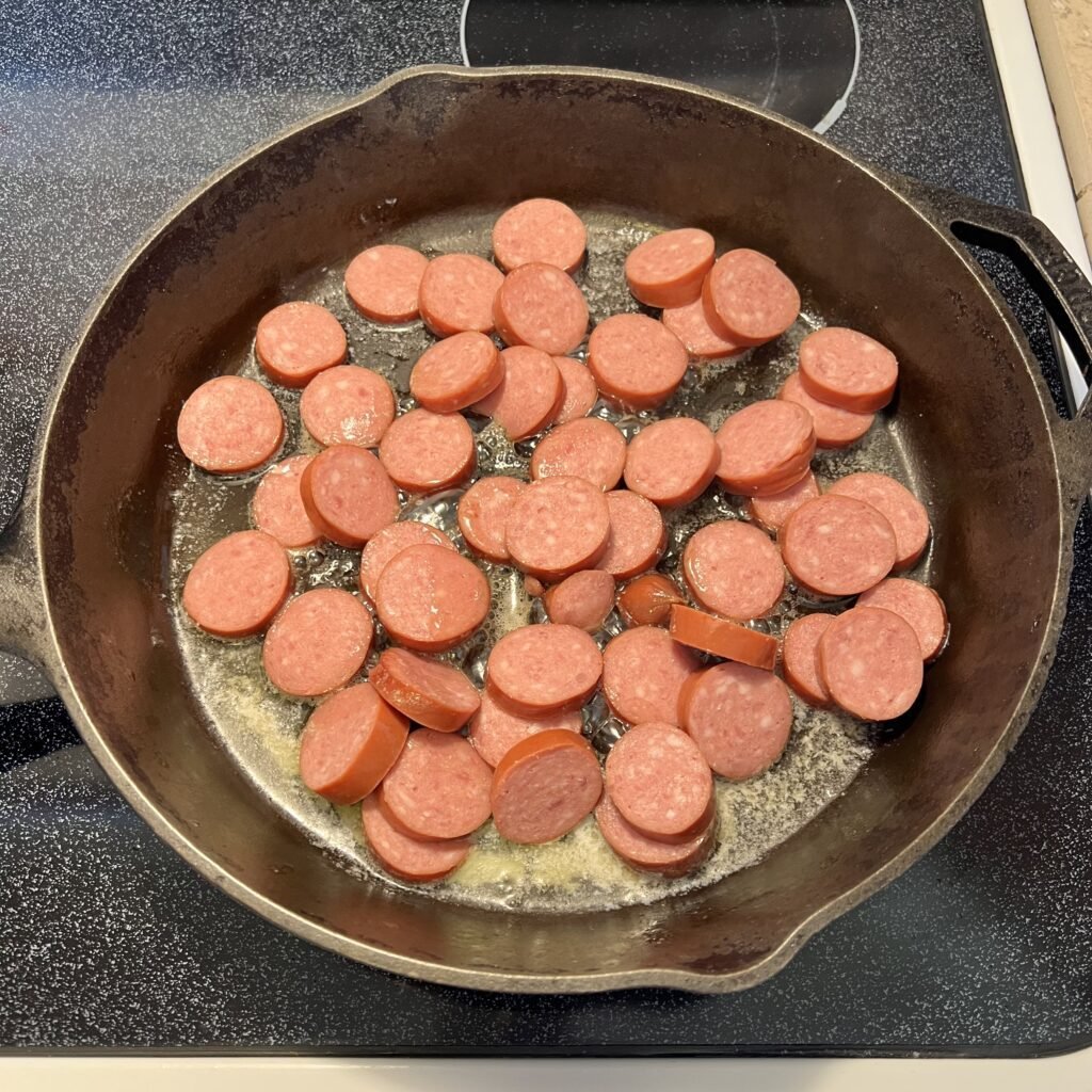 Kielbasa sausage slices heating up in a skillet.