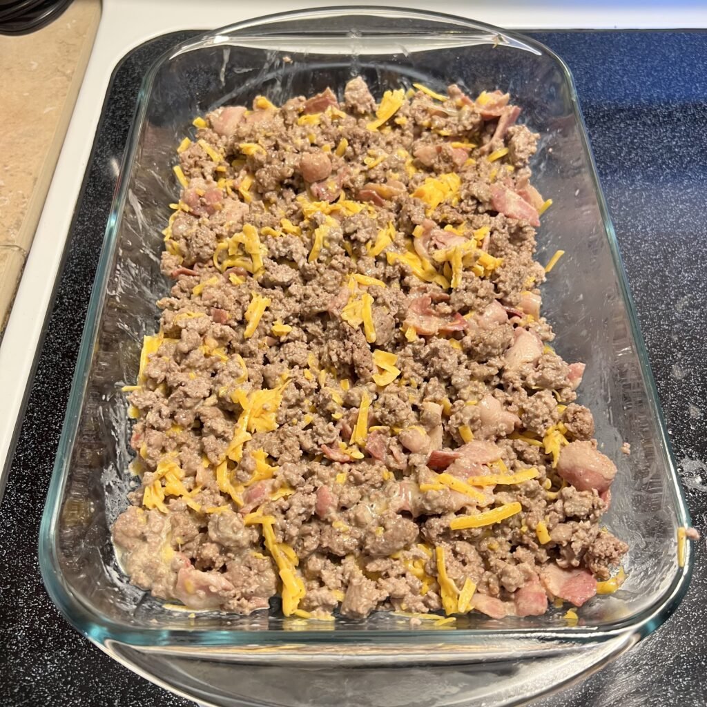Mixed carnivore casserole ingredients in a prepared 9x13 baking dish.