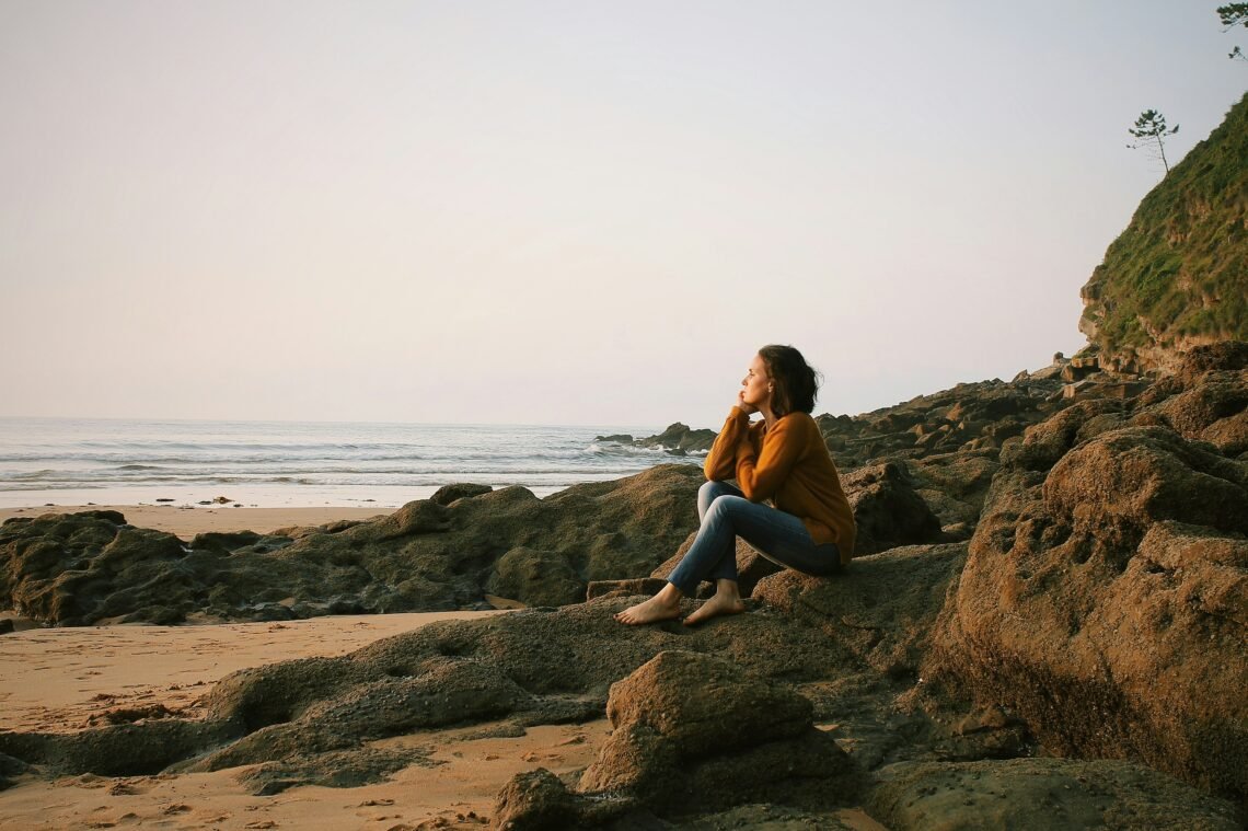 A woman peacefully sitting on the beach.