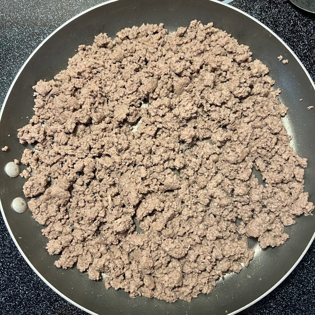 Overhead shot of browned ground beef in a large frying pan. Ready for delicious Alfredo sauce to be poured over the top for a super easy 2-ingredient meal.