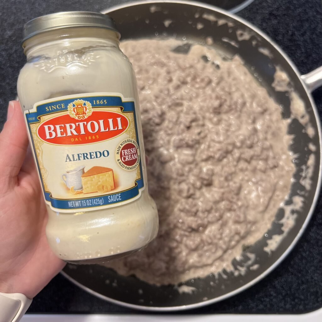 An overhead shot of a jar of Bertolli Alfredo sauce with a frying pan of the sauce and ground beef in the background. A simple and family-friendly 2-ingredient meal.