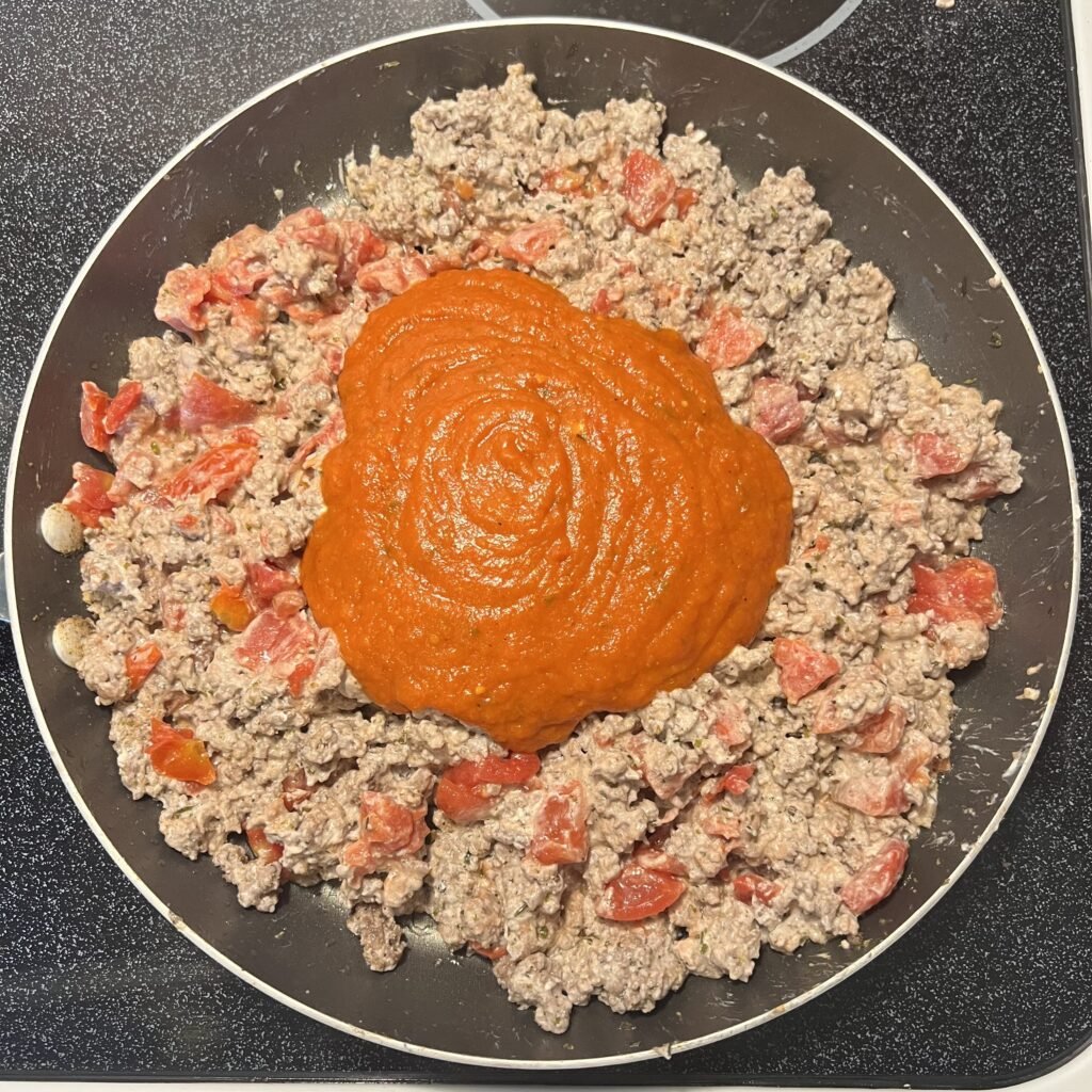 Creamy ground beef with tomatoes and marinara in a frying pan on the stove.