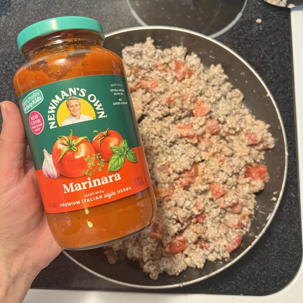 A jar of Newman's Own Marinara sauce with creamy ground beef and tomatoes in the background.