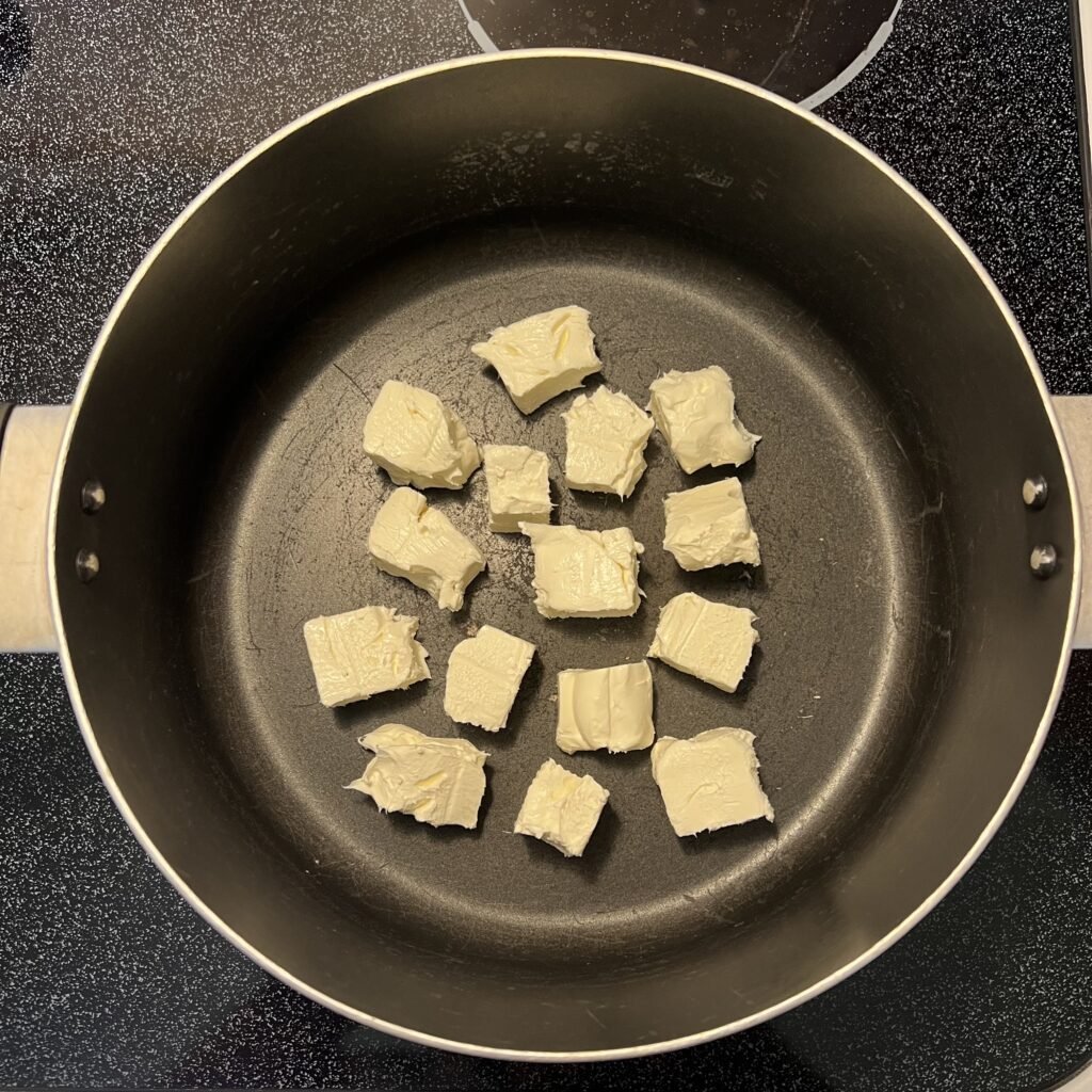 An overhead shot of a soup pot with cubed and softened cream cheese ready to be melted.