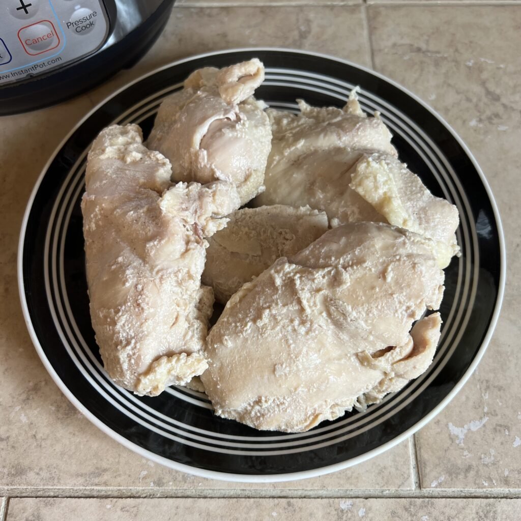 Freshly cooked chicken breasts on a plate next to the instant pot.