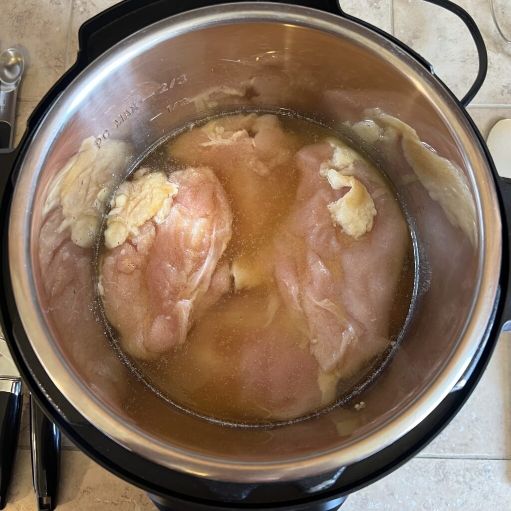 Seasoned chicken breasts and chicken broth in an instant pot ready to be quickly cooked for a delicious meal.
