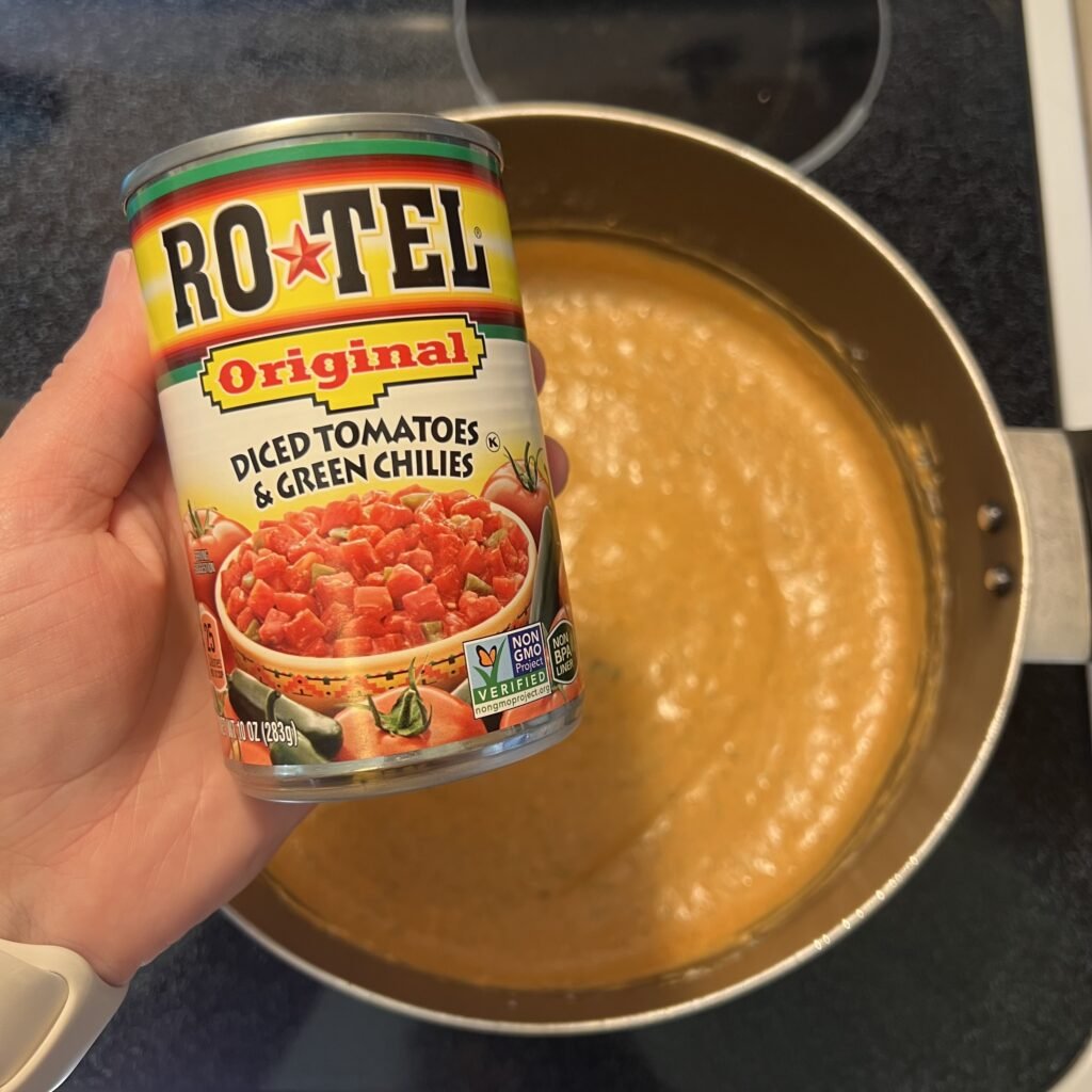 A close-up shot of a can of Rotel with a pot of cream cheese marinara sauce in the background.