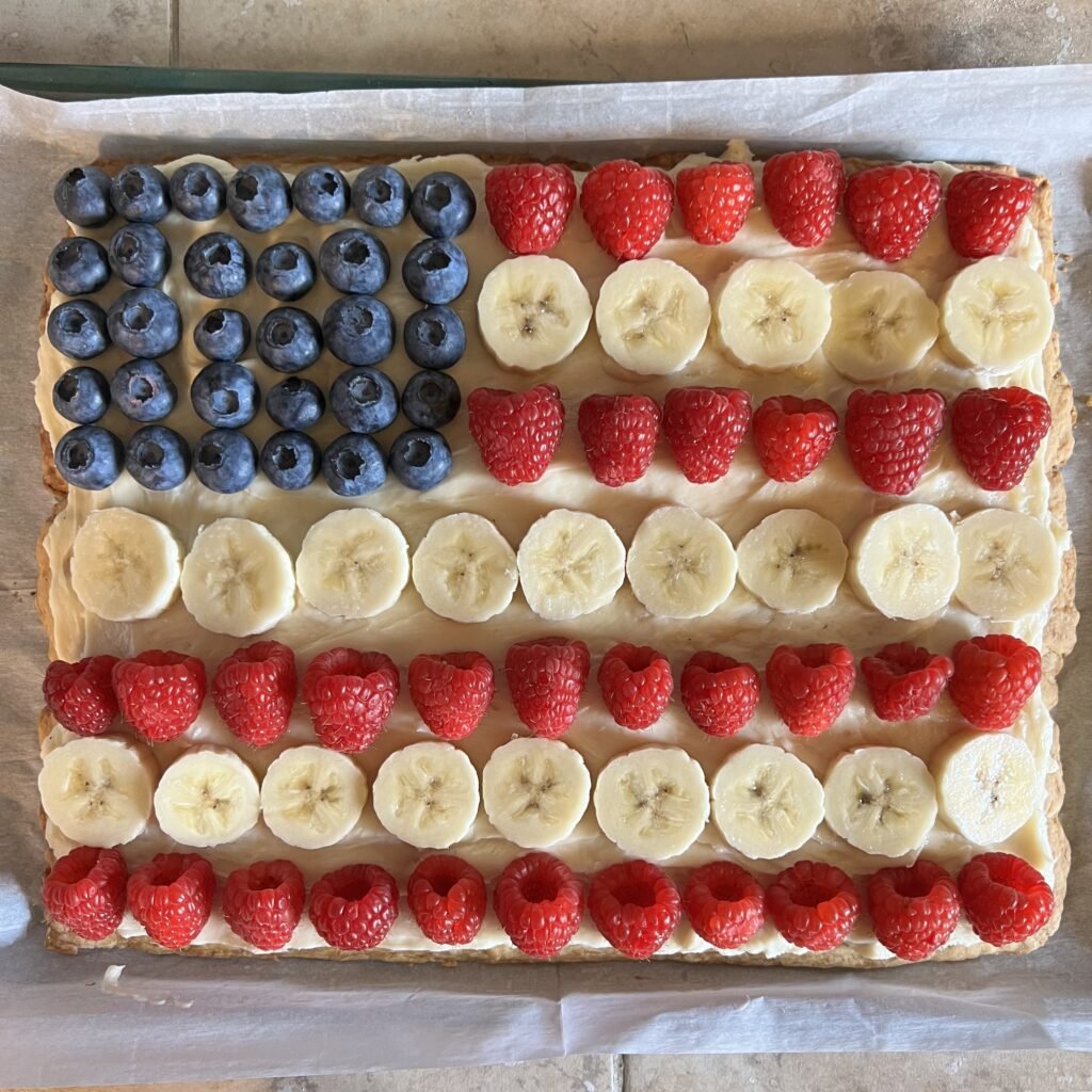 An over-head shot of a sourdough sugar cookie fruit pizza decorated like the American flag to celebrate our great nation. It is on a parchment-lined baking sheet. Reynolds parchment paper sheets are a must-have in the kitchen!
