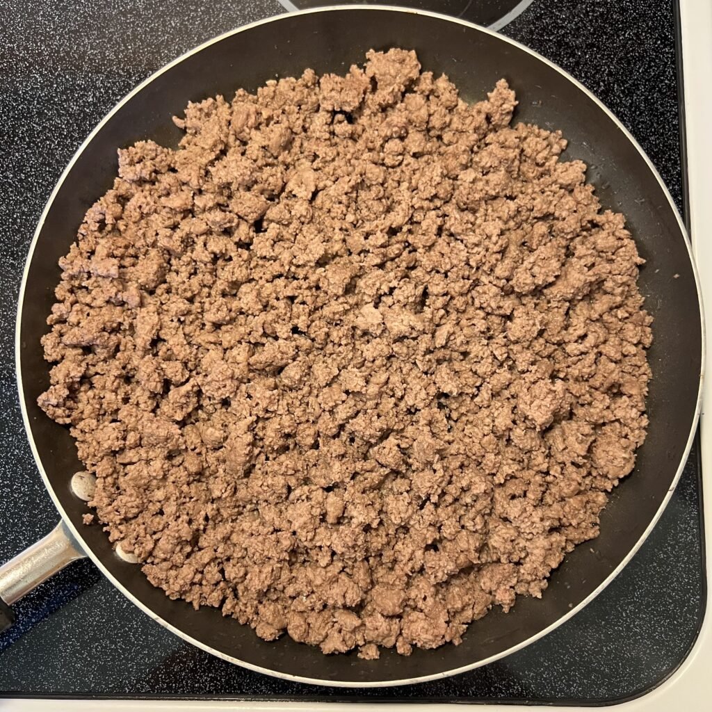 An overhead shot of browned ground beef in a frying pan on the stove.