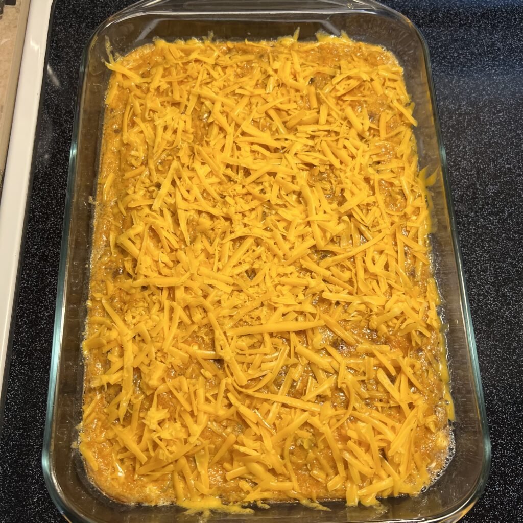 A mostly baked casserole topped with extra shredded cheddar cheese ready to finish baking.