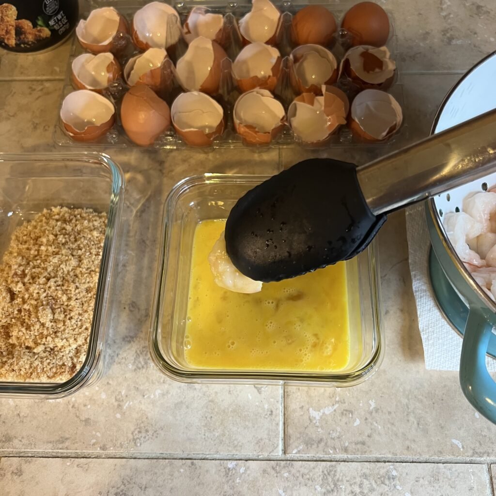 Dipping shrimp into whisked eggs as the first step for coating them before frying.