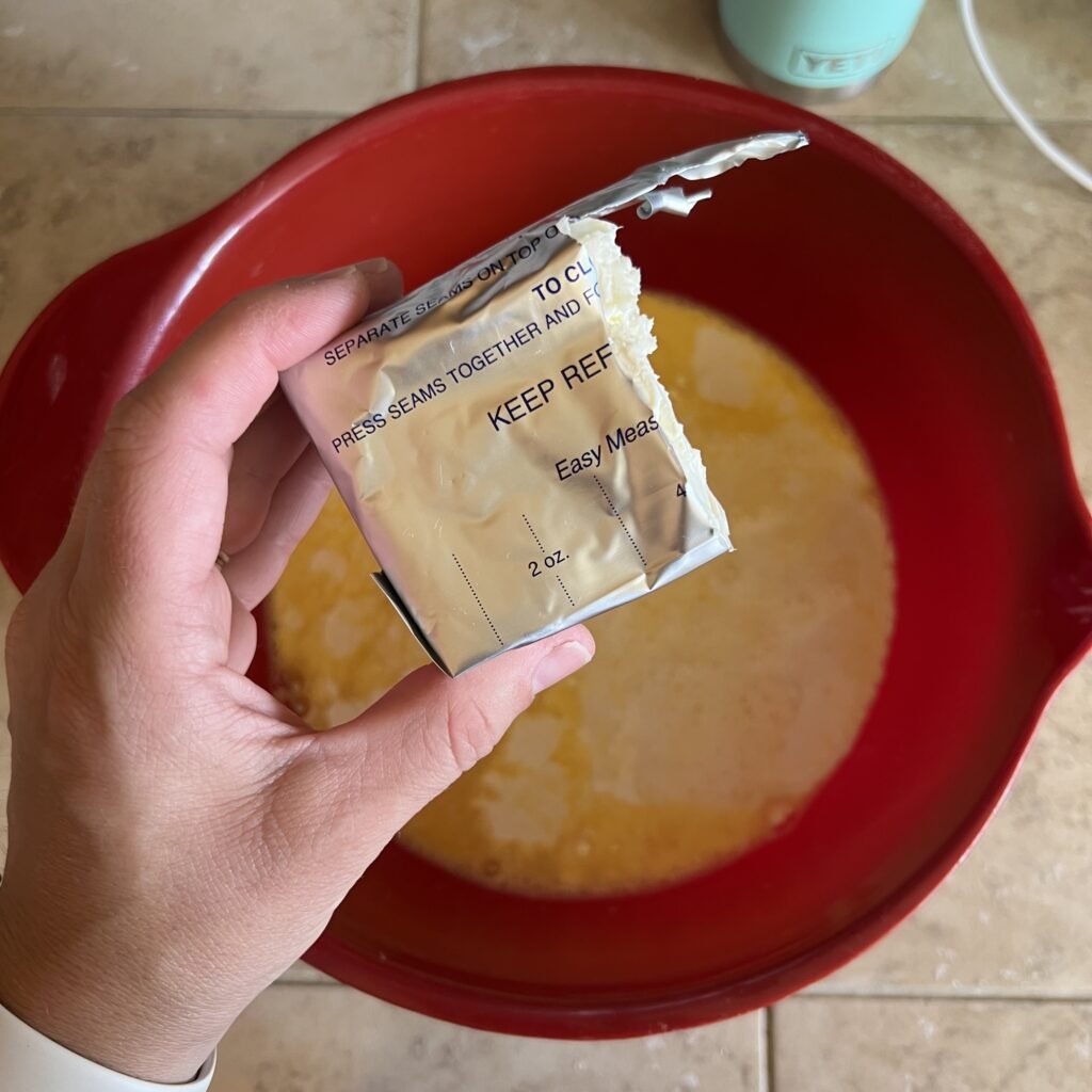 An overhead shot of 4 ounces of cream cheese above a bowl of scrambled eggs and cream in preparation of making an easy dinner casserole.
