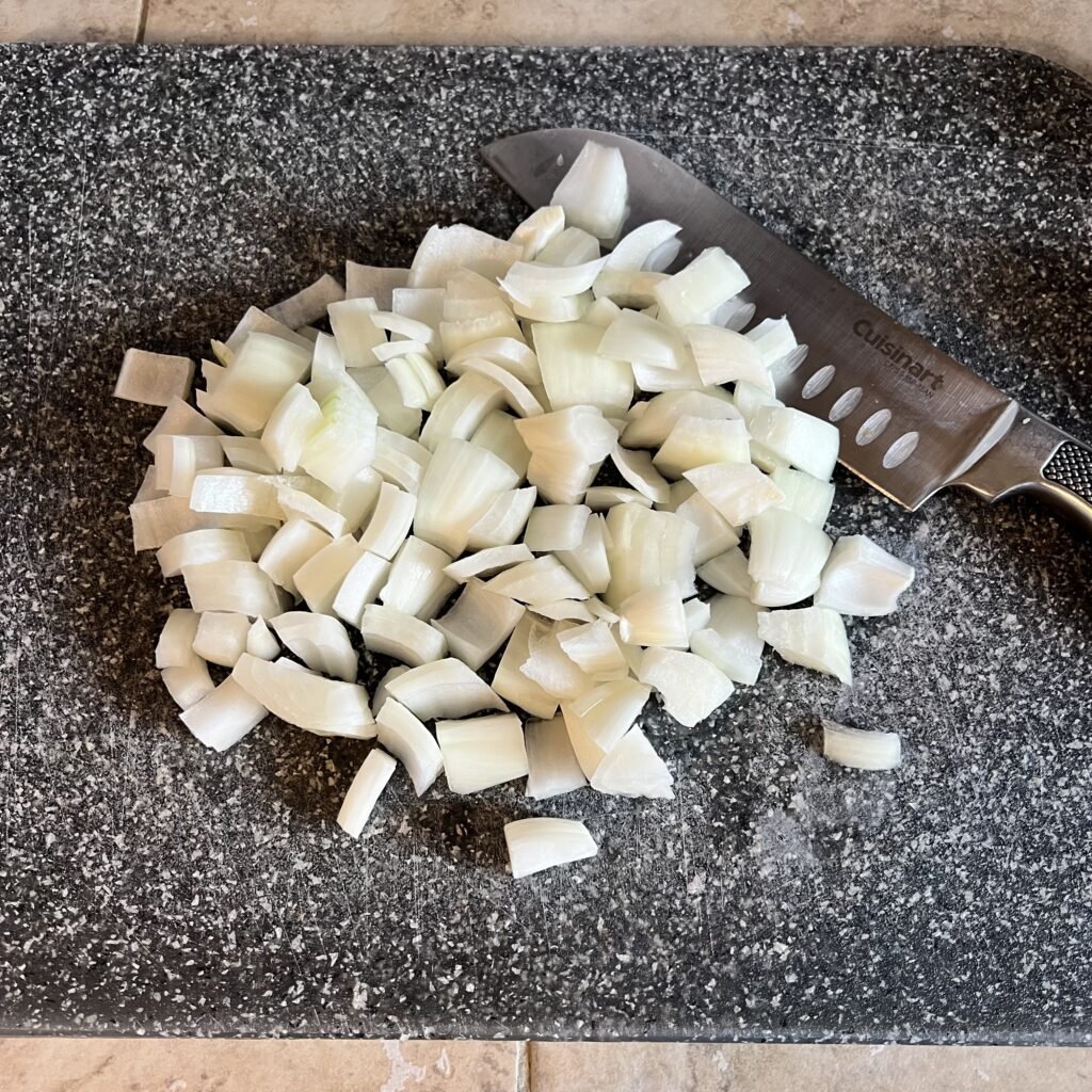 An close-up shot of a cutting board, Cuisinart knife, and diced onions. A cutting board and a quality knife set are must-haves on any kitchen essentials for moms list.