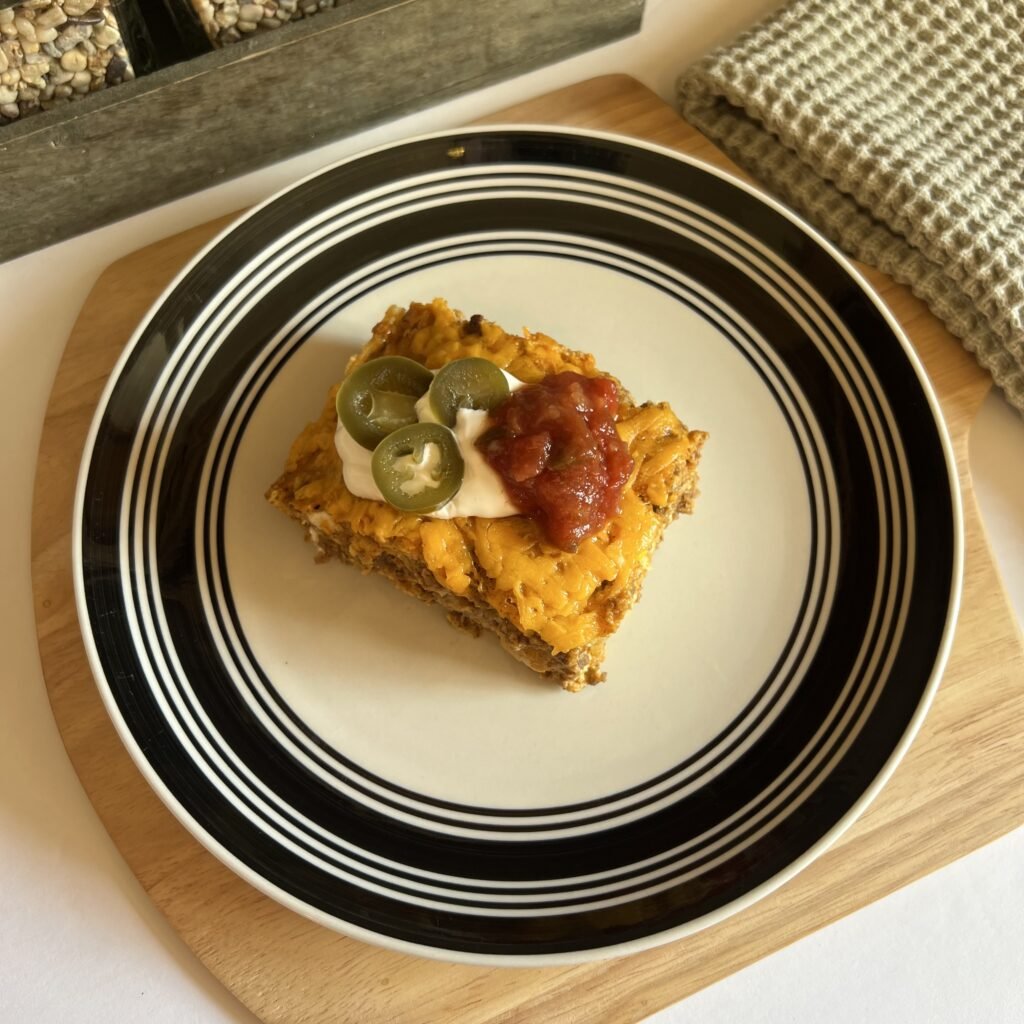 An overhead shot of a slice of easy taco casserole topped with spicy salsa, pickled jalapeños, and a dollop of sour cream.