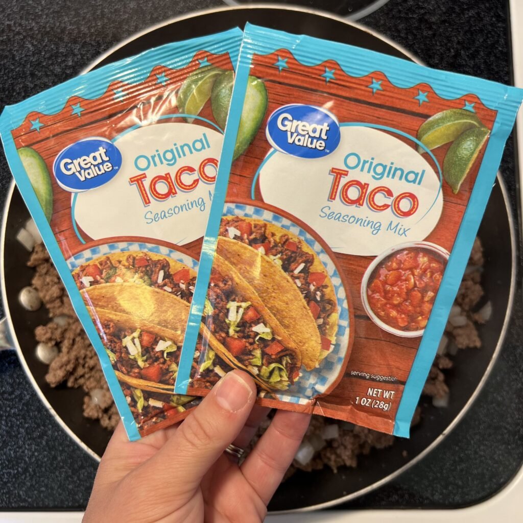 Two packets of Great Value Original Taco Seasoning Mix over a pan of ground beef and onions, ready to make delicious taco meat.