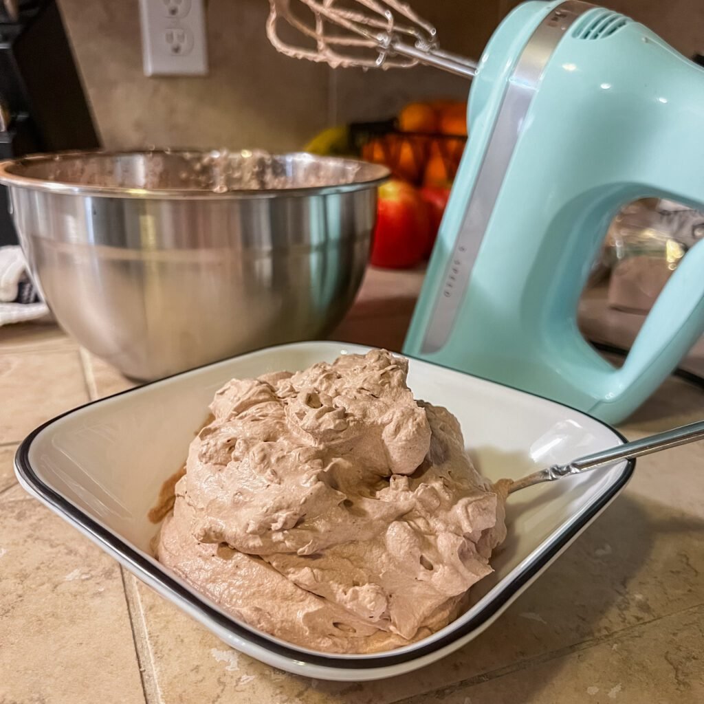 A close-up of homemade 3-ingredient chocolate mousse with a Kitchen Aid hand mixer in the background. The Kitchen Aid hand mixer is part of the list of Kitchen Essentials for Moms.