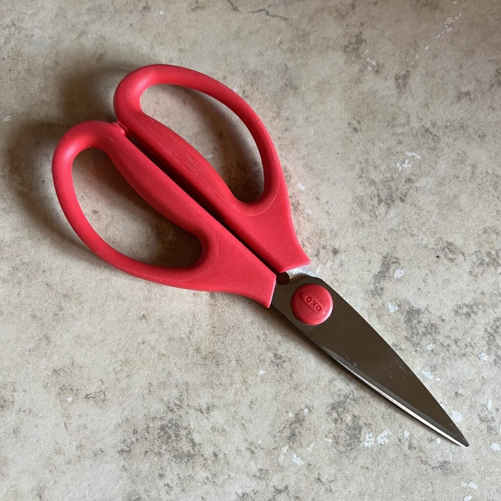 Red-handled OXO kitchen scissors come in handy for preparing meat and cutting open tough packages. These are a must on any kitchen essentials for moms list.