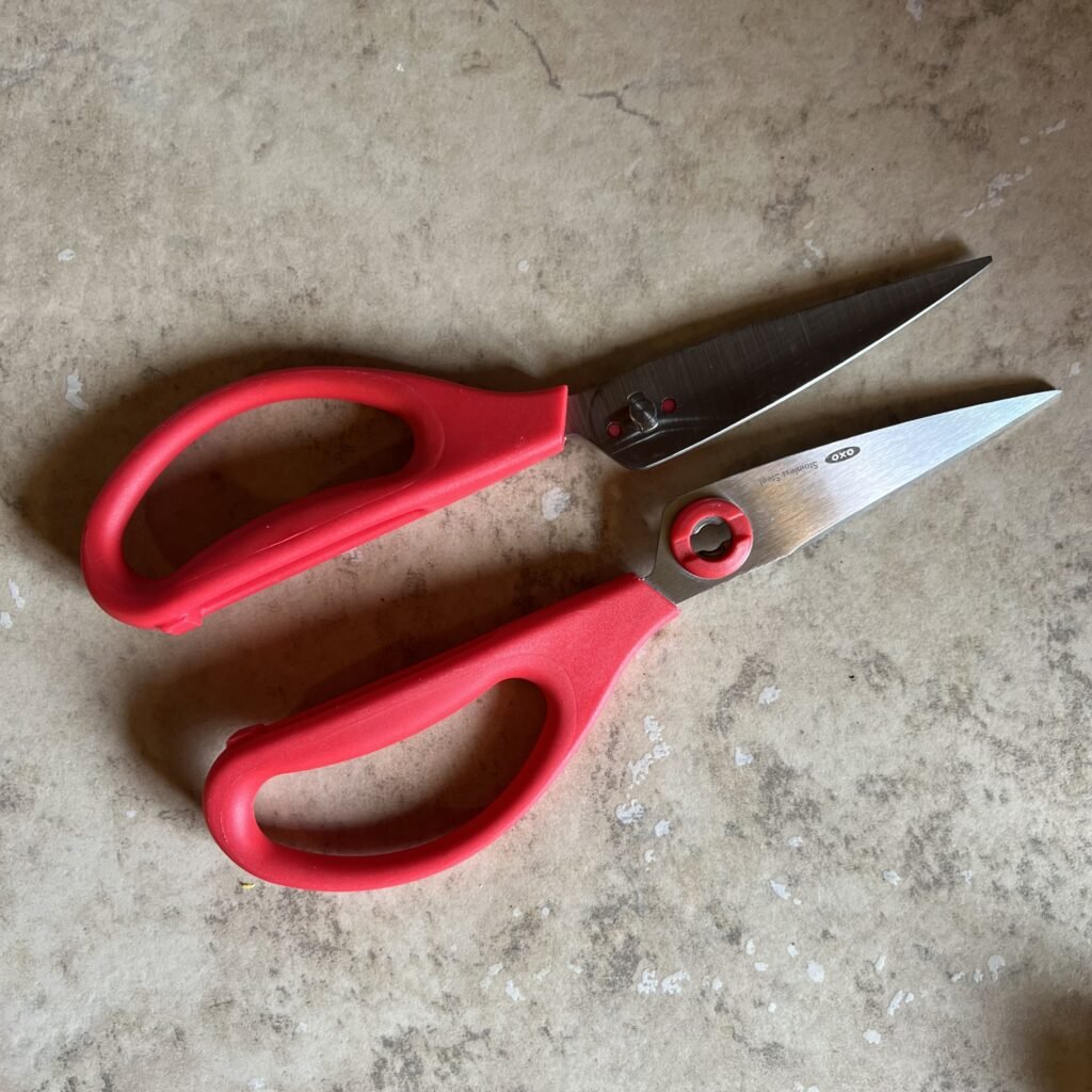 Red-handled OXO kitchen shears pulled apart, showing that the scissors easily come apart for full cleaning after use.