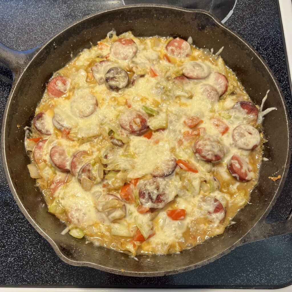 An overhead shot of a cheesy kielbasa and cabbage skillet cooked in a cast iron skillet.