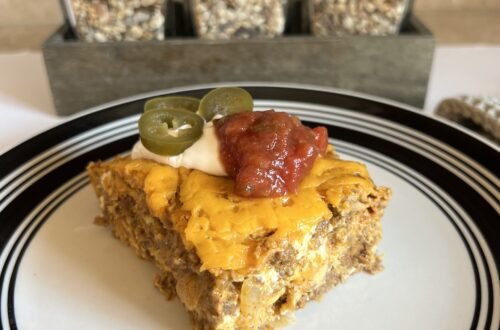 A side shot of a slice of delicious taco casserole topped with sour cream, jalapeños, and spicy salsa.