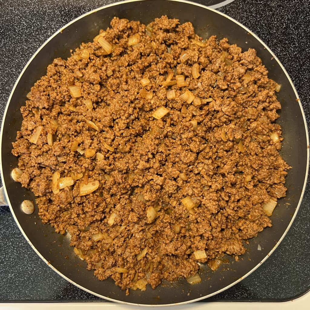 Cooked taco meat with onions in a frying pan on the stovetop.