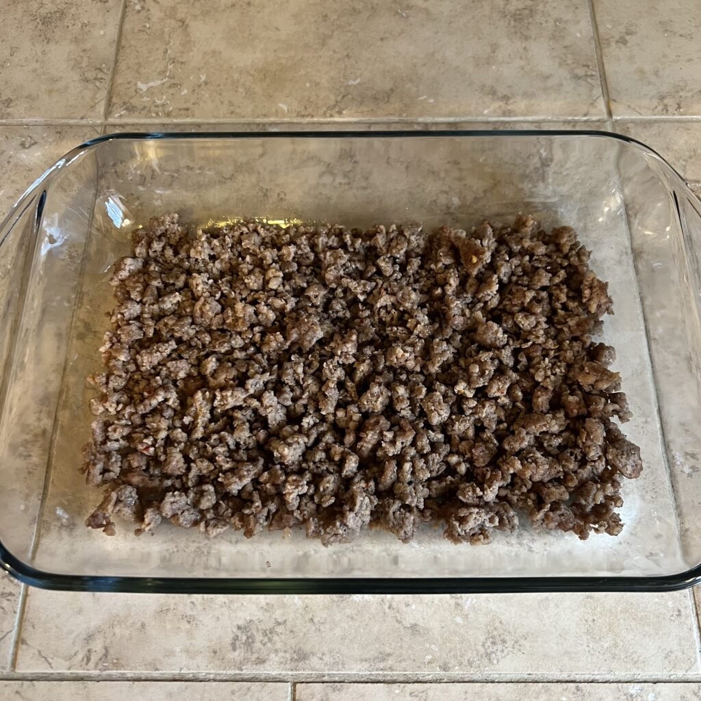 Cook ground breakfast sausage in a glass baking dish. This is the first layer in this sausage and egg casserole.