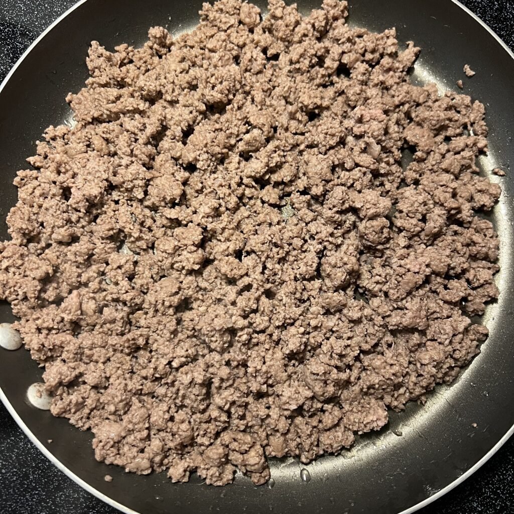 A close-up shot of ground beef browning in a frying pan. This is step one to making a Creamy Salsa Verde Ground Beef Skillet.