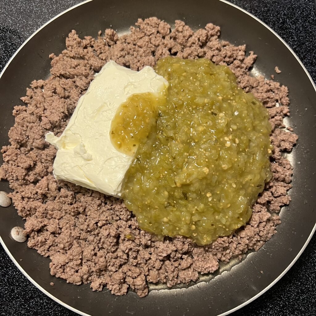 A close-up shot of browned ground beef with cream cheese and salsa verde added to the top.