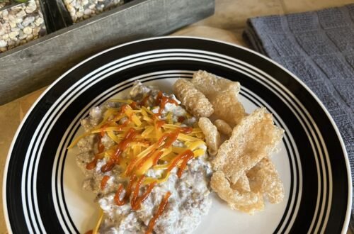 A delicious plate of creamy salsa verde ground beef served with shredded cheddar, sriracha sauce, and pork rinds.