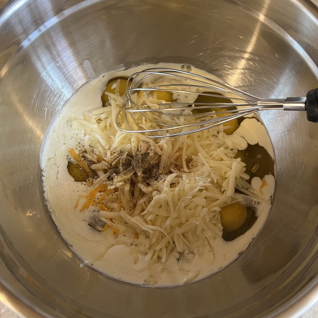 The keto breakfast casserole egg mixture ingredients in a mixing bowl with a wisk, ready to be mixed together.