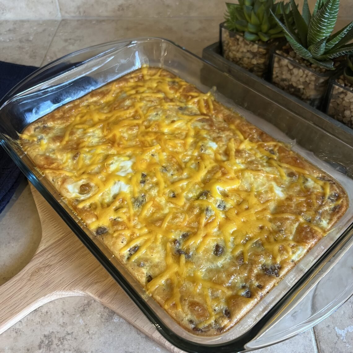 A side shot of a freshly baked keto breakfast casserole on the count with a blue towel and succulent plants in the background.