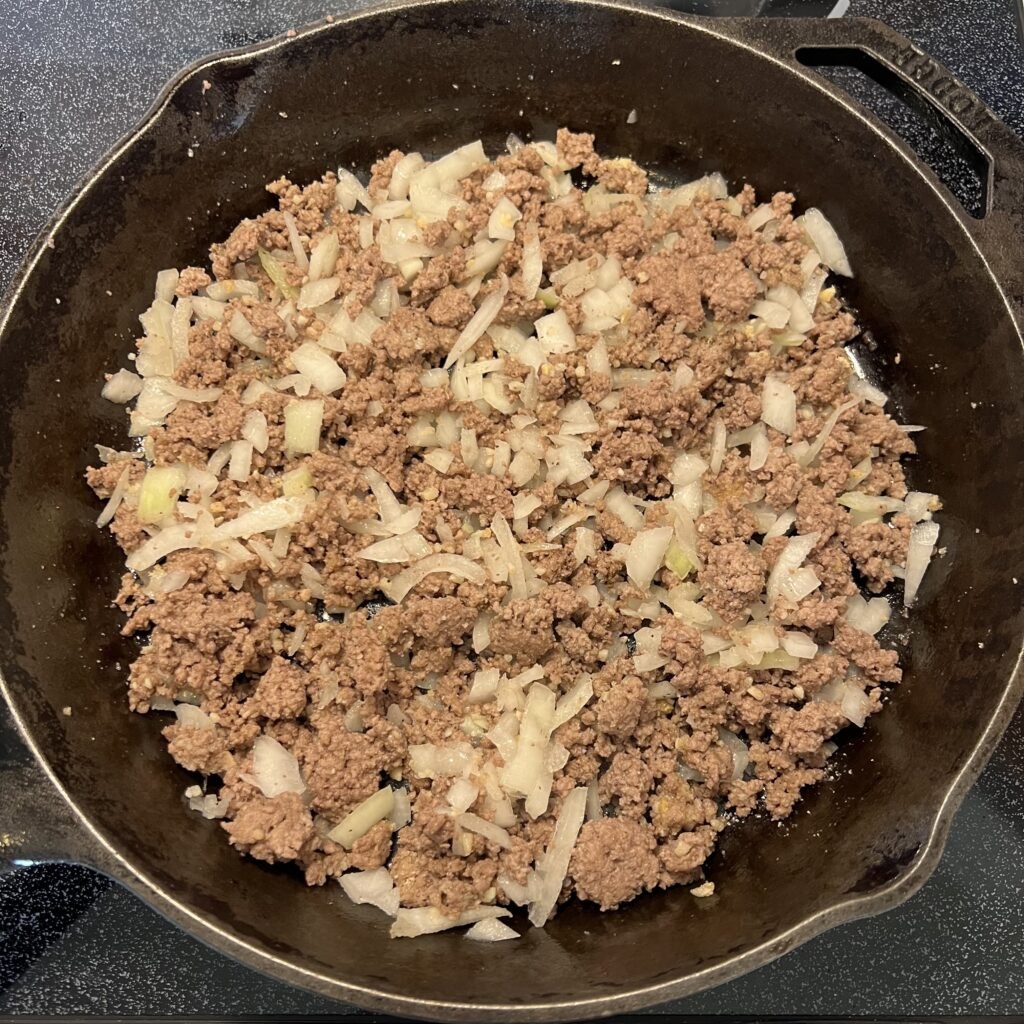 Browned burger and onion in a cast iron skillet on the stove top.