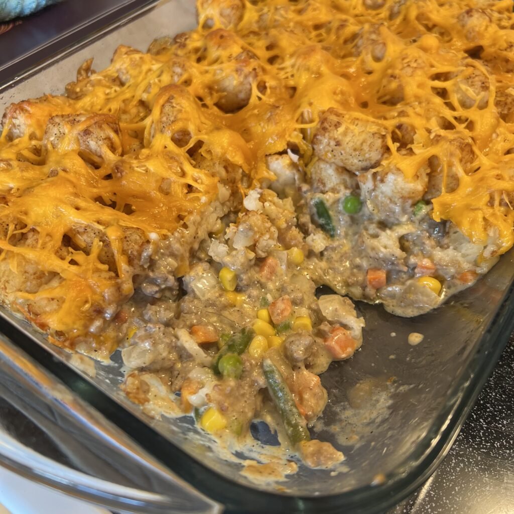A close-up of a pan of delicious family hot dish with a portion scooped out so you can see the creamy veggie and beef filling.
