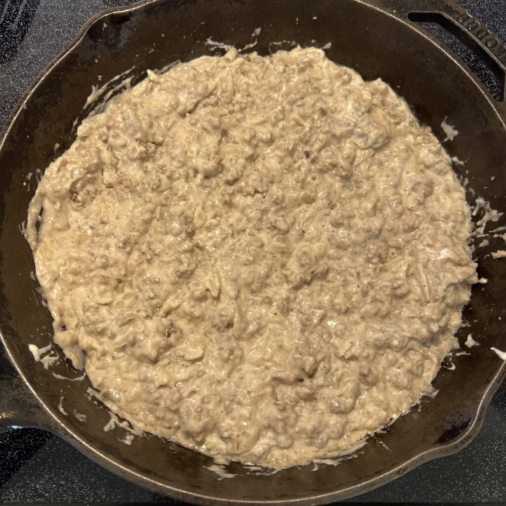 A close-up shot of the first part of tater tot casserole filling heating up in a cast iron skillet.