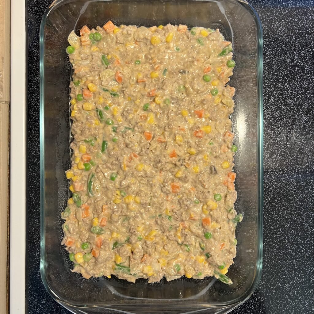 Tater tot hot dish filling in a 9x13 baking dish, the first step to assembling this delicious dinner.