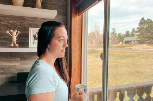 A busy mom standing by the window, finding rest in Jesus.